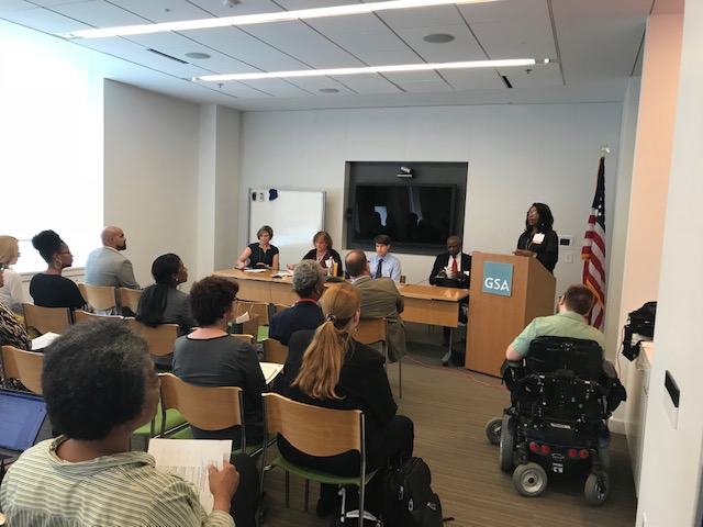 Arnetta White of NAVAIR stands at a podium, introducing panelists in front of a conference room full of forum attendees.