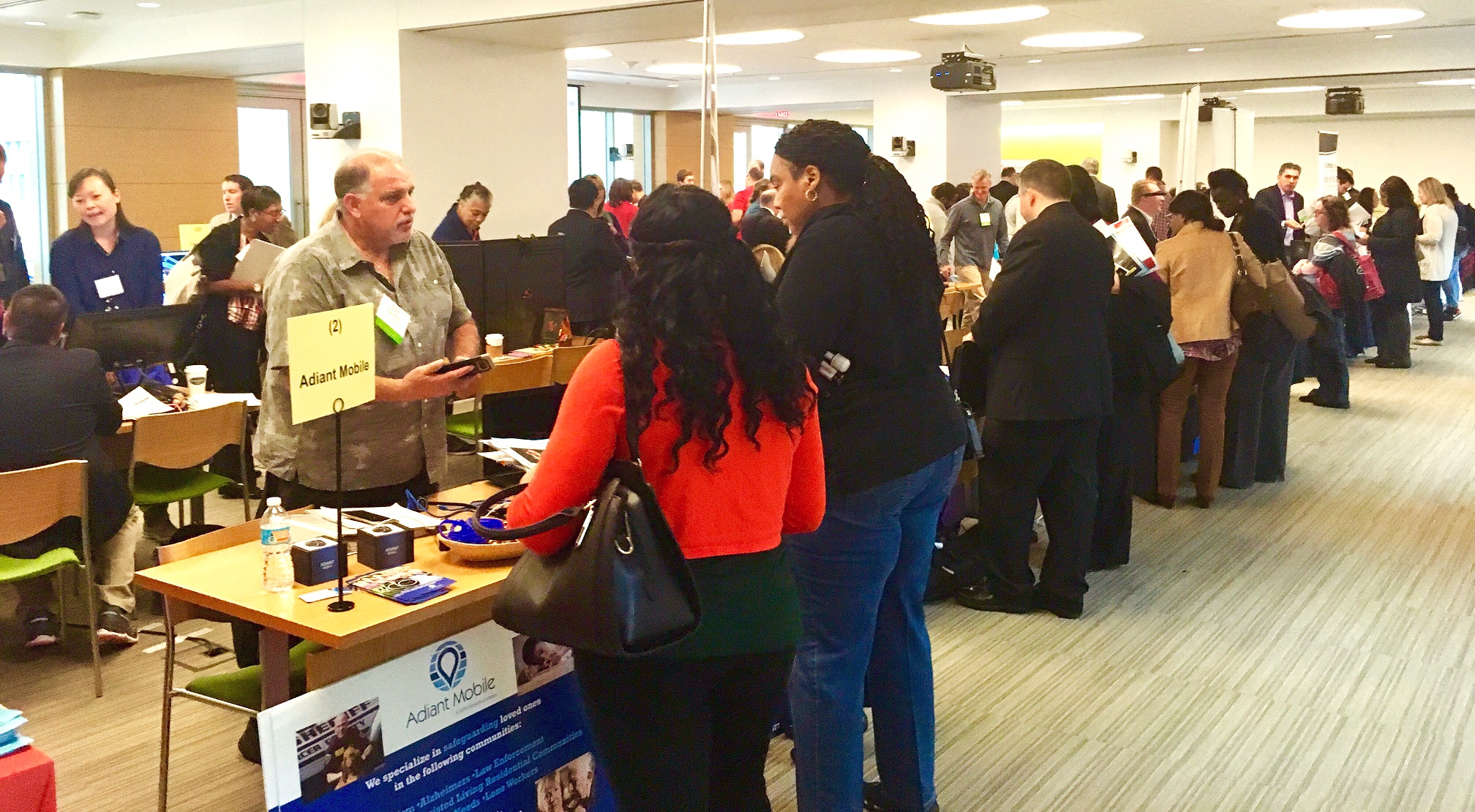 Photo showing vendors behind tables displaying technology services, and event attendees examining the technology and speaking to vendors